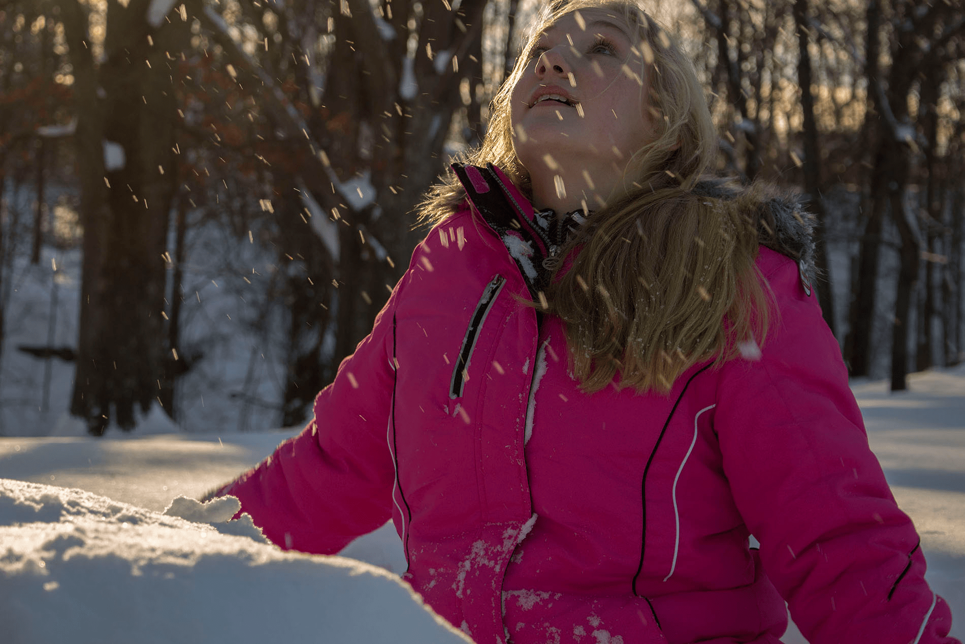 An image of a girl looking at falling snow in sunlight.